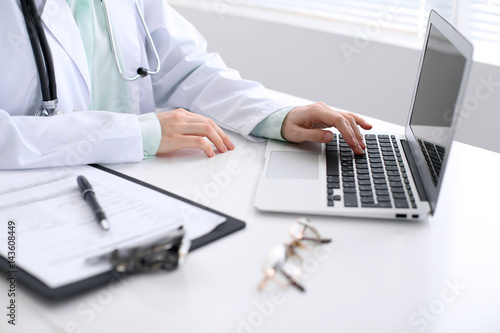 Close-up of a female doctor typing on laptop computer  sitting at the table in the hospital