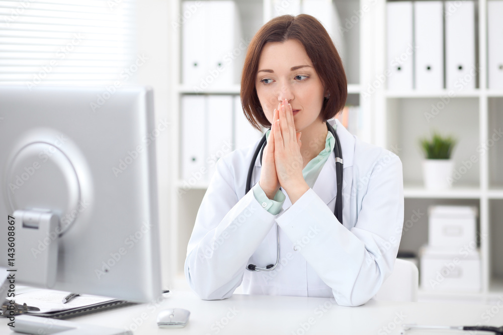 Young brunette female doctor sitting at a desk and working on the computer at the hospital office. Health care, insurance and help concept. Physician ready to examine patient Young brunette female doctor sitting at a desk and working on the computer at the hospital office. Health care, insurance and help concept. Physician ready to examine patient