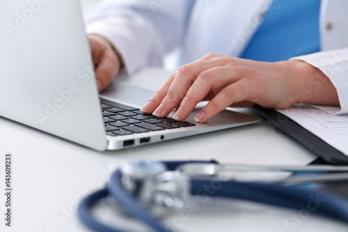 Close up of unknown female doctor typing on laptop computer while sitting at the table. Medical staff, compulsory work concept