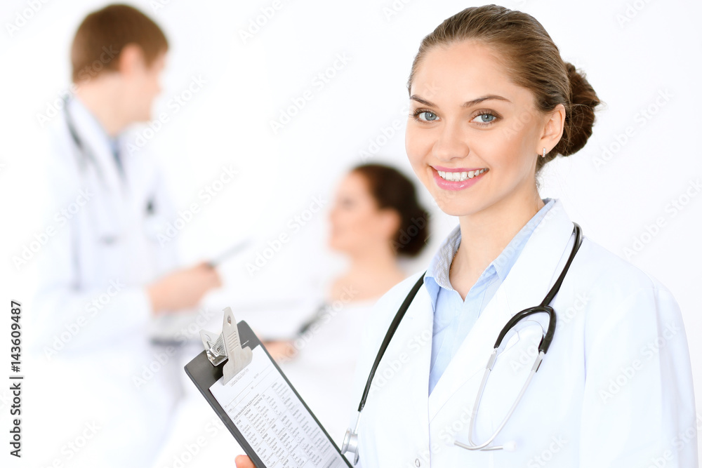 Cheerful smiling female doctor on the background with physician and his patient in the bed. High level and quality of medical service concept. Cheerful smiling female doctor on the background with physician and his patient in the bed. High level and quality of medical service concept.