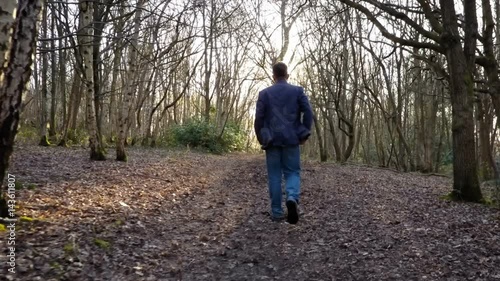 Forest walk; man walking into sunlight on a woodland path - rear following drone