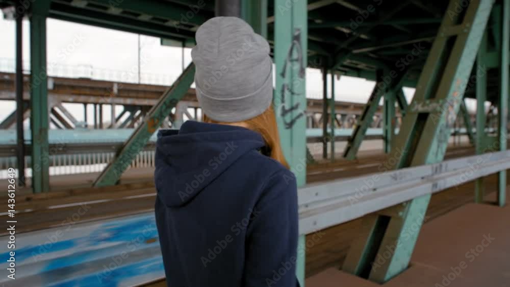 Nice Young Girl in Cap is Going Quickly across Industrial Transport Bridge in the City Nice Young Girl in Cap is Going Quickly across Industrial Transport Bridge in the City