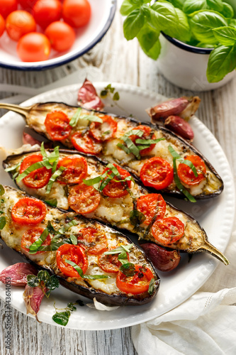 Griled eggplants with cheese, cherry tomatoes and basil on white plate