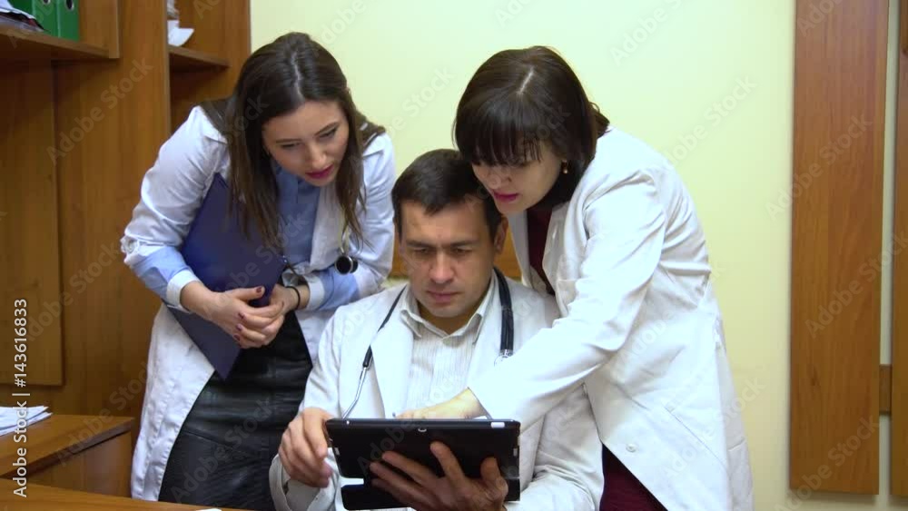 A group of doctors talking. Two women and a man. Male doctor keep a tablet. A group of doctors talking. Two women and a man. Male doctor keep a tablet.