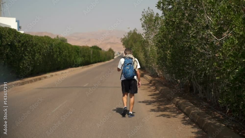 Young man walking by the road with backpack slow motion Young man walking by the road with backpack slow motion