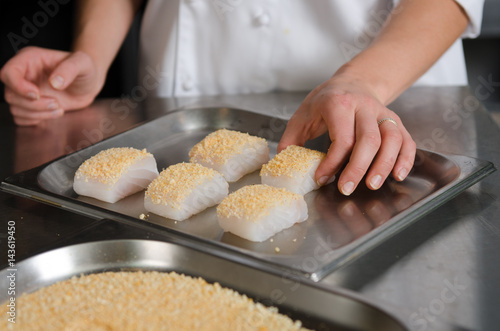 Fresh fish fillet cube covered in breadcrumbs, being placed onto a metal baking tray.
