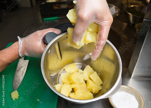 Close up shot of a hand dropping fluffy peeled potatoes into a blender.