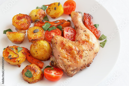 roasted chicken leg with potato, pumpkin, and cherry tomatoes decorated with cilantro and pumpkin seeds