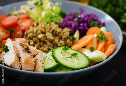 Healthy salad with chicken, tomatoes, cucumber, lettuce, carrot, celery, red cabbage and mung bean on dark background. Proper nutrition. Dietary menu.