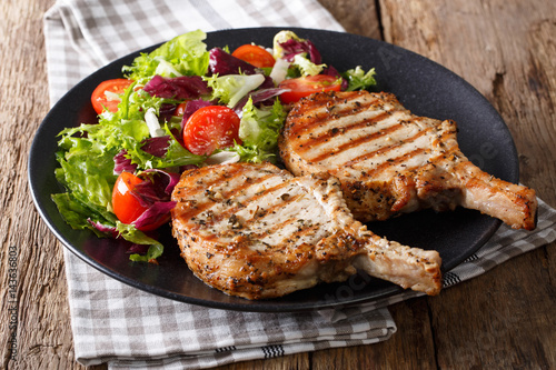 Grilled pork steak with bone, fresh vegetable salad close-up. Horizontal