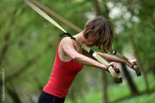 Young woman does suspension training with fitness straps in the outdoors