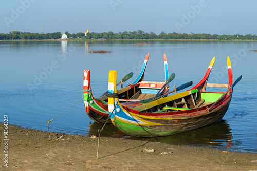 Fototapeta Naklejka Na Ścianę i Meble -  Two colored traditional Burmese boats on the shore of Taung Tha Man lake. Amarapura, Myanmar