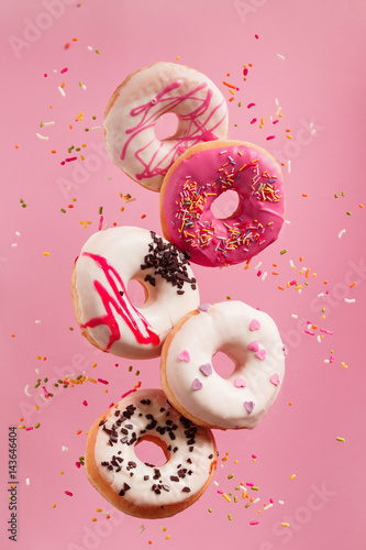 Various decorated doughnuts in motion falling on pink background.