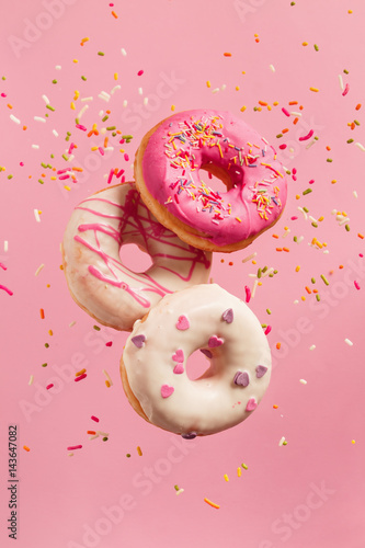 Photo Various decorated doughnuts in motion falling on pink background.