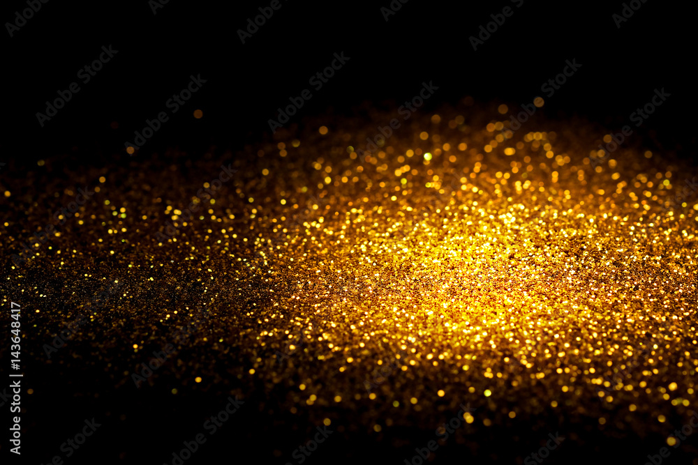 Fototapeta premium Sprinkle gold glitter dust on a black background with copy space.