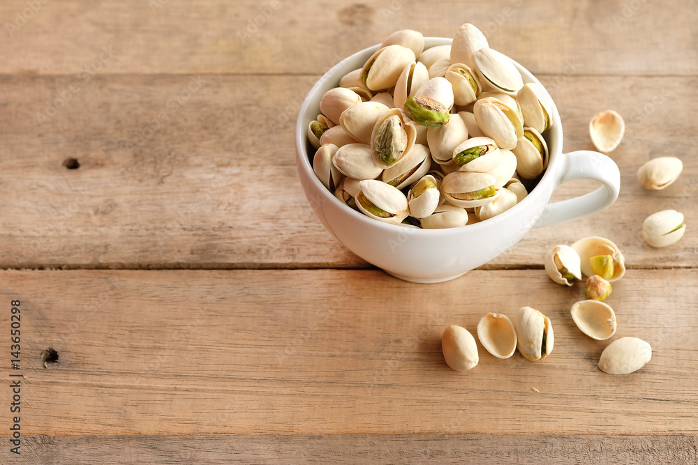 Pistachios are dried in a white cup on a wooden background. Pistachios are dried in a white cup on a wooden background.