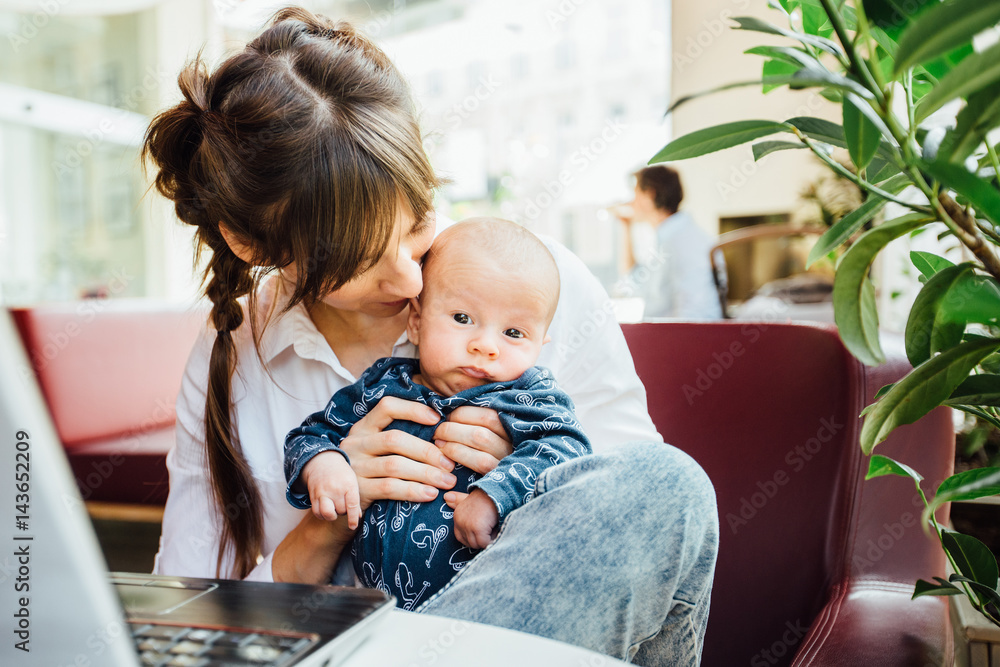 Beautiful young mother working with laptop computer and breastfeeding, holding and nursing her newborn baby at cafe. Mom - business woman feeding newborn. Beautiful young mother working with laptop computer and breastfeeding, holding and nursing her newborn baby at cafe. Mom - business woman feeding newborn.