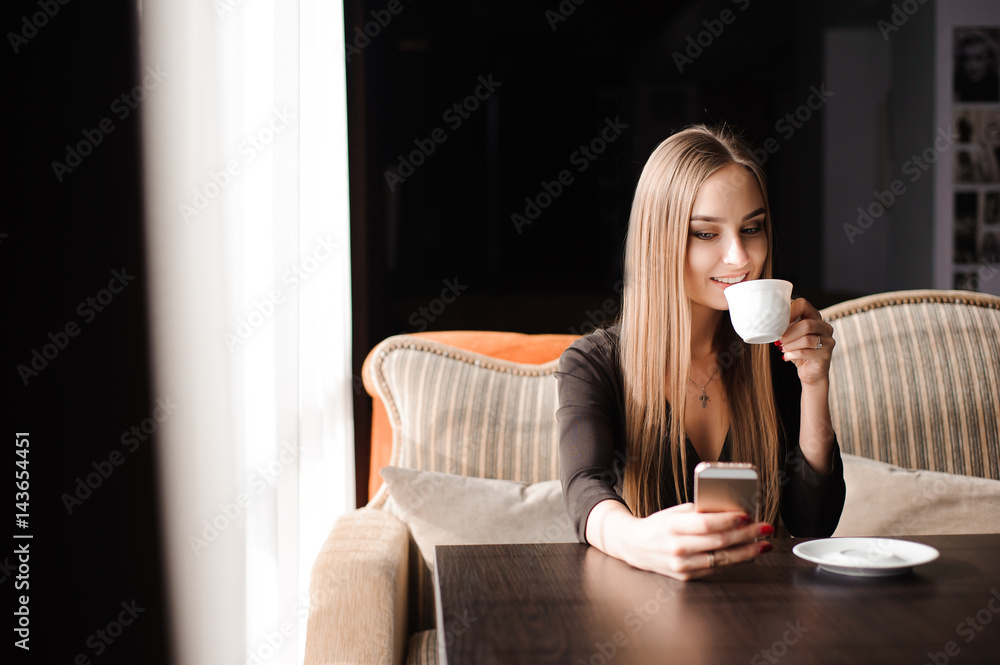 Young woman drinking coffee in a cafe and using a mobile phone Young woman drinking coffee in a cafe and using a mobile phone