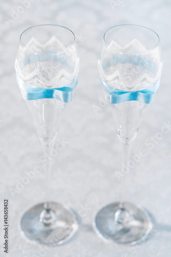 Glasses of wine glasses. The transparent glasses are decorated with white lace and blue ribbon. Vertical frame, selective focus.