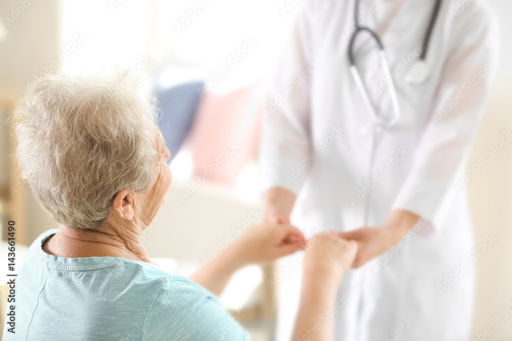 Fototapeta premium Young doctor holding hands of elderly woman on light background