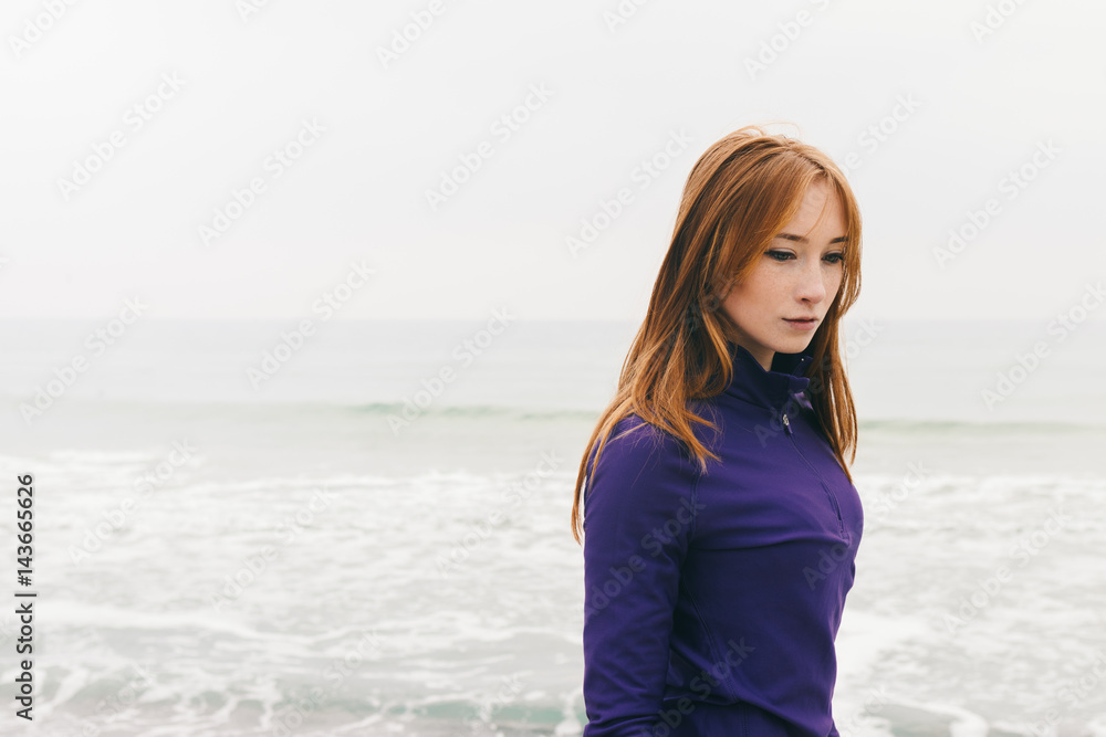 Pensive beautiful young red-haired girl on the beach on a cloudy day Pensive beautiful young red-haired girl on the beach on a cloudy day