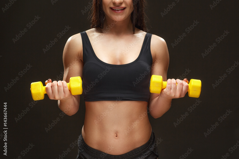 Working on her biceps. Cropped shot of a muscular woman working out with the dumbbells smiling against black background at the studio. Working on her biceps. Cropped shot of a muscular woman working out with the dumbbells smiling against black background at the studio.