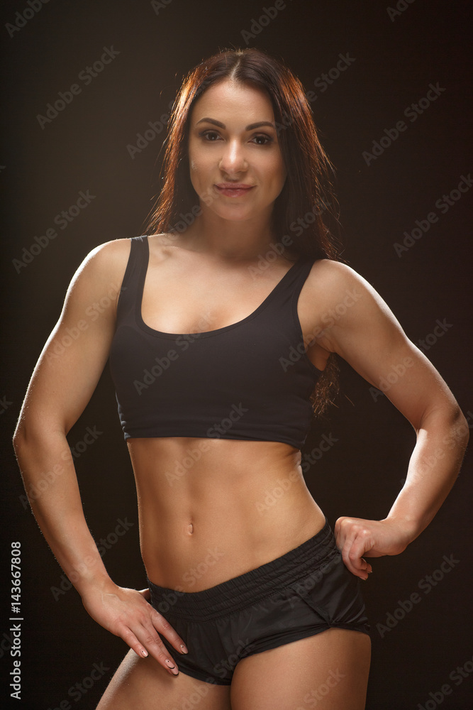 Confident in her success. Vertical studio shot of a sporty brunette wearing black top and shorts posing looking to the camera against black background. Confident in her success. Vertical studio shot of a sporty brunette wearing black top and shorts posing looking to the camera against black background.