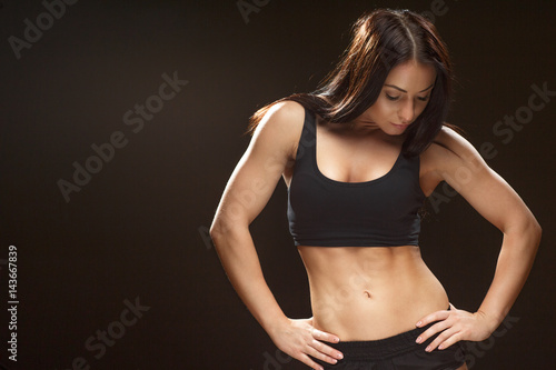 In great progress. Studio shot of an attractive female athlete posing at the studio looking down on her abs copyspace on the side on black background.