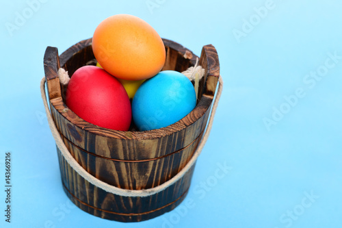 painted easter colorful eggs in wooden bucket on blue background