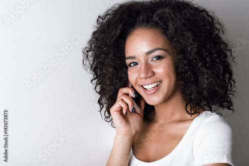 Cheerful young brunette talking on phone, standing at wall with copy space