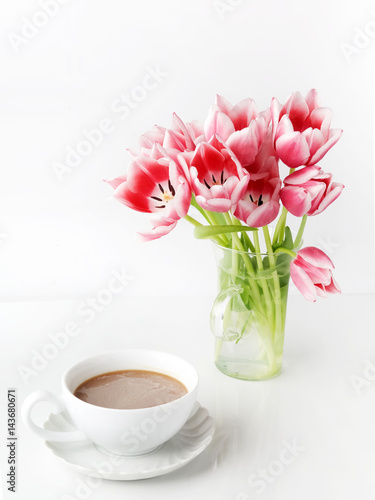 Tulips in glass and coffee cup on white table.