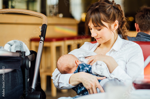 Obraz na płótnie A young mother is breastfeeding her baby in a cafe while she is having a tea tim