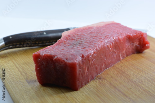 Raw steak on a chopping board with a steak knife next to it