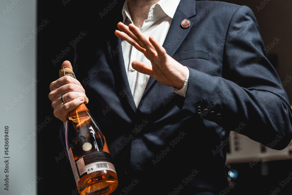 Fototapeta premium Sommelier in a dark blue jacket holding a bottle of wine and tells the audience about the various wines