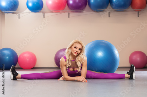 Sport woman sits on a twine. Athletic girl doing stretching exercise in the fitness room