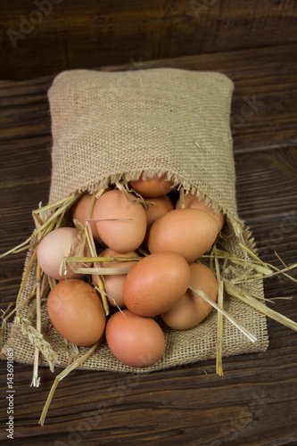 Chicken eggs with straw in bag on wooden background