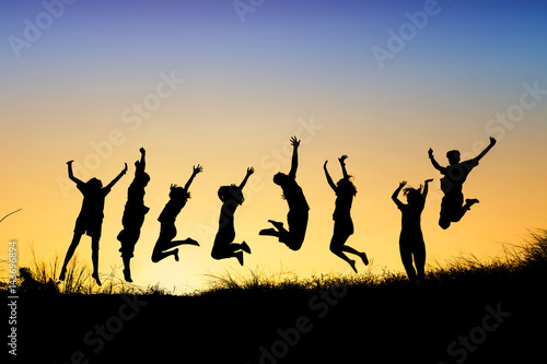 Silhouettes of young group of people jumping on the hill