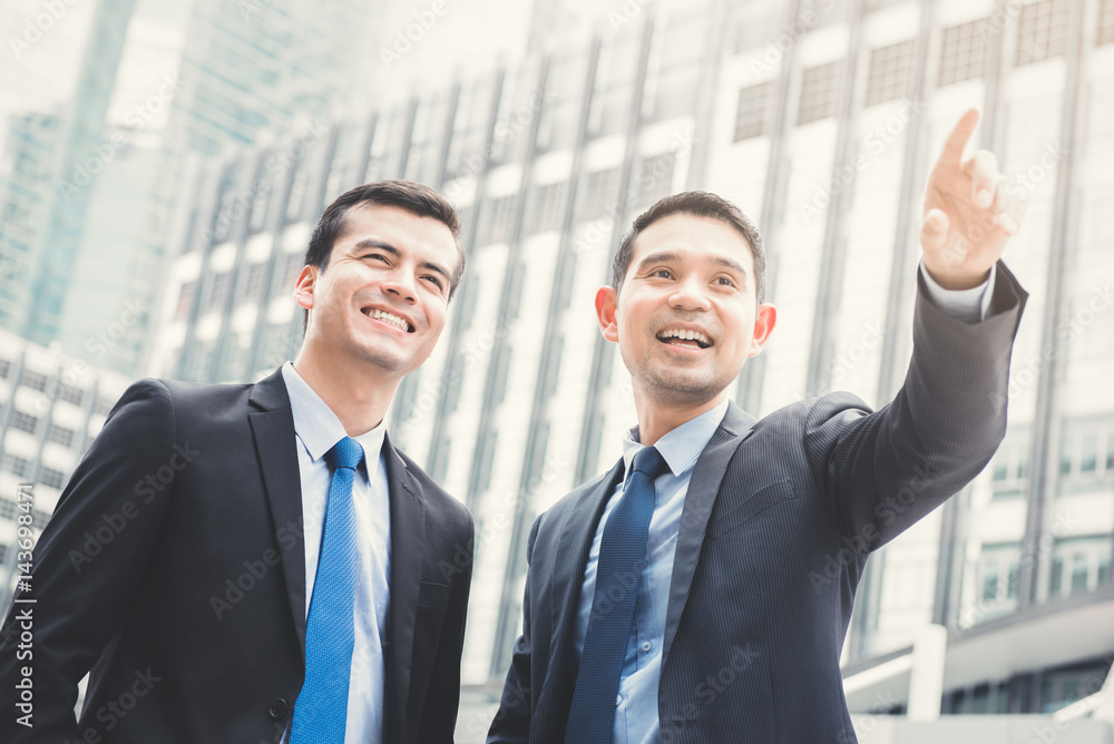 Two businessmen standing outdoors in the city with one hand pointing out Two businessmen standing outdoors in the city with one hand pointing out