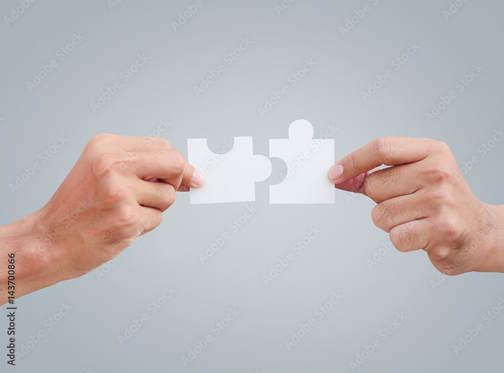Cropped hands of businessmen joining jigsaw pieces on gray background Cropped hands of businessmen joining jigsaw pieces on gray background