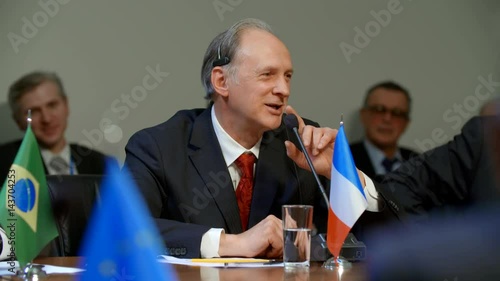 French participant of international congress or summit. Polititian man smiles, jokes, starts his speech photo