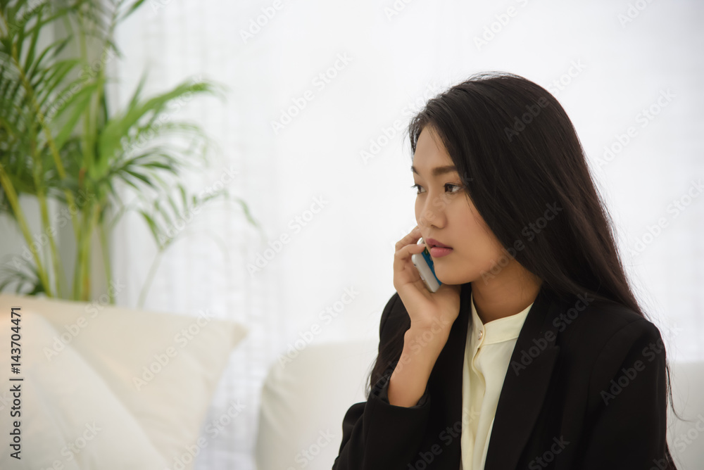 Elegant young business woman talking on the mobile phone sitting on white sofa