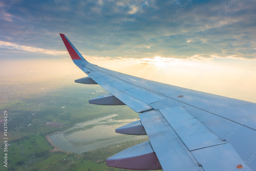 Fototapeta premium Wing of an airplane flying above the clouds at sunset .