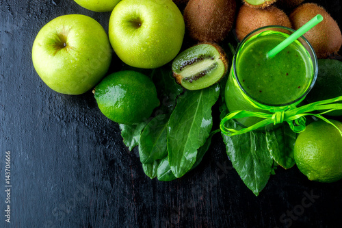 Green smoothie near ingredients for it on black wooden background. Apple, lime, spinach, kiwi. Detox. Healthy drink. Top view. Copy space.