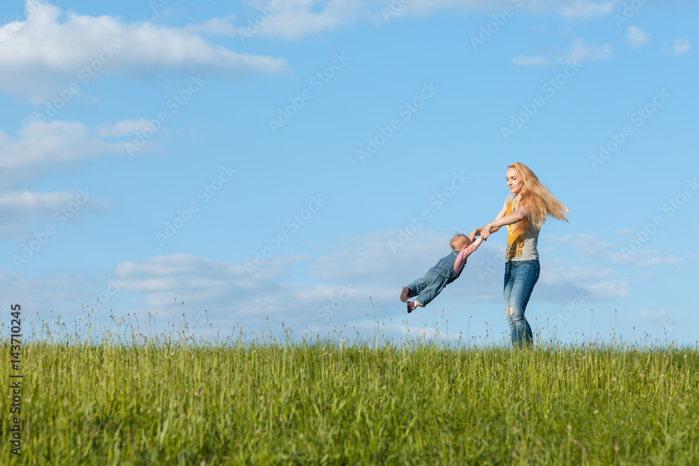 Young mother walking with her baby. Mom is circling her child by the hands Young mother walking with her baby. Mom is circling her child by the hands