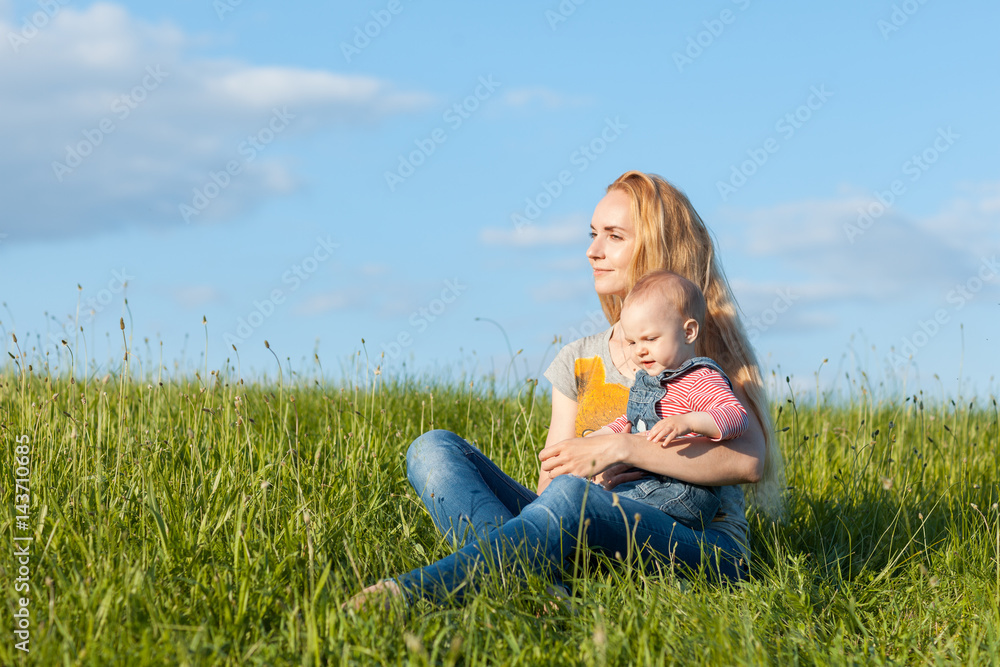 Young mother sitting in the grass and holding a child Young mother sitting in the grass and holding a child
