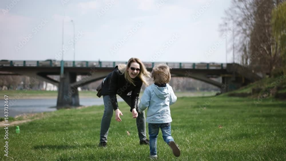 Child Running Into Mother's Hands to Hug Her and Spinning Around. Family Having Fun in the Park on a Green Grass. Slow Motion Child Running Into Mother's Hands to Hug Her and Spinning Around. Family Having Fun in the Park on a Green Grass. Slow Motion