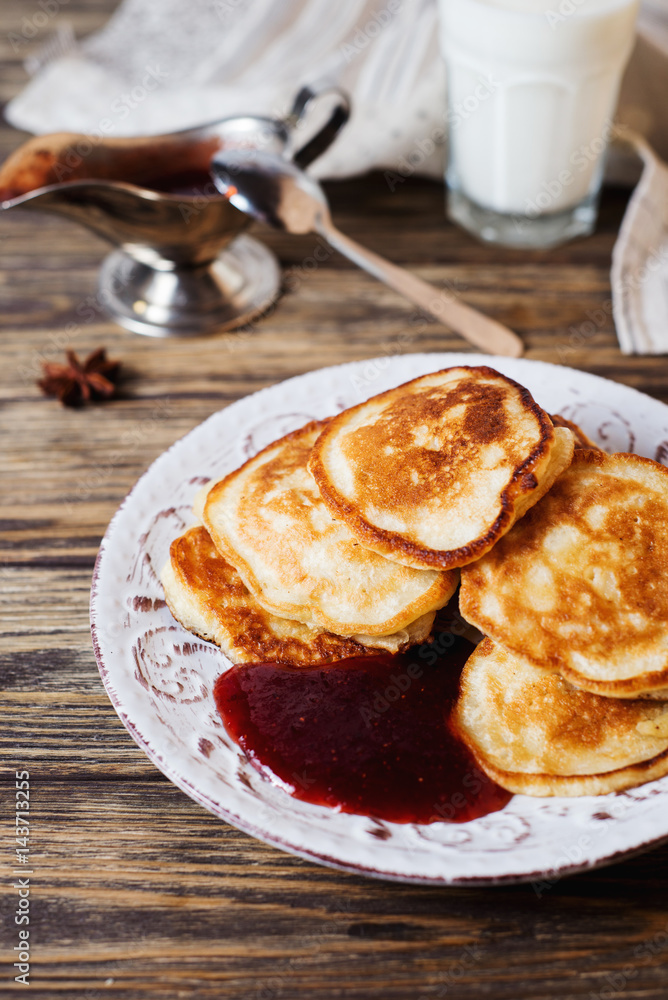Hearty and tasty breakfast or lunch, fried pancakes with strawberry jam, milk and black tea on a dark wooden background Hearty and tasty breakfast or lunch, fried pancakes with strawberry jam, milk and black tea on a dark wooden background