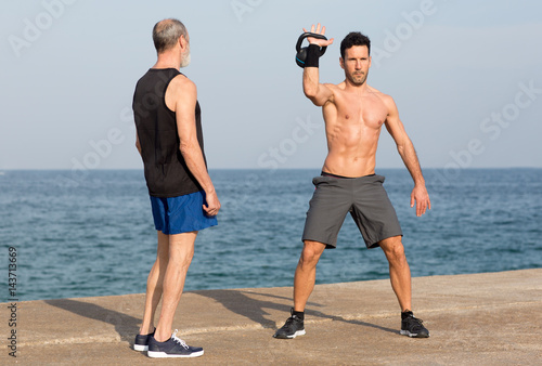 Athletischer Mann macht Training mit Kettlebell am Meer und Coach photo