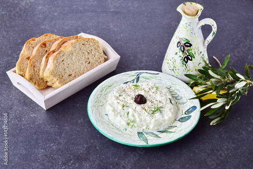 Greek traditional sauce tzatziki with olives, olive oil jar, lemon and bread on a grey abstract background. Healthy eating concept