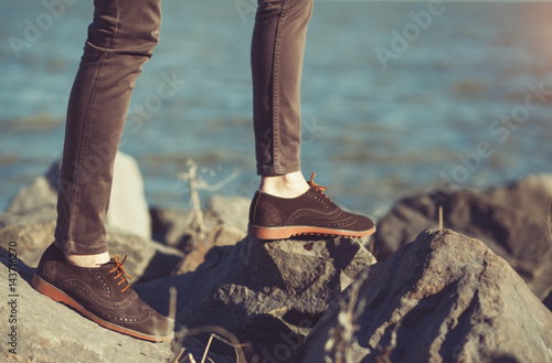 Vintage photo of fashion hipster man's foot in brown leather suede shoes walking on the stones in spring day.